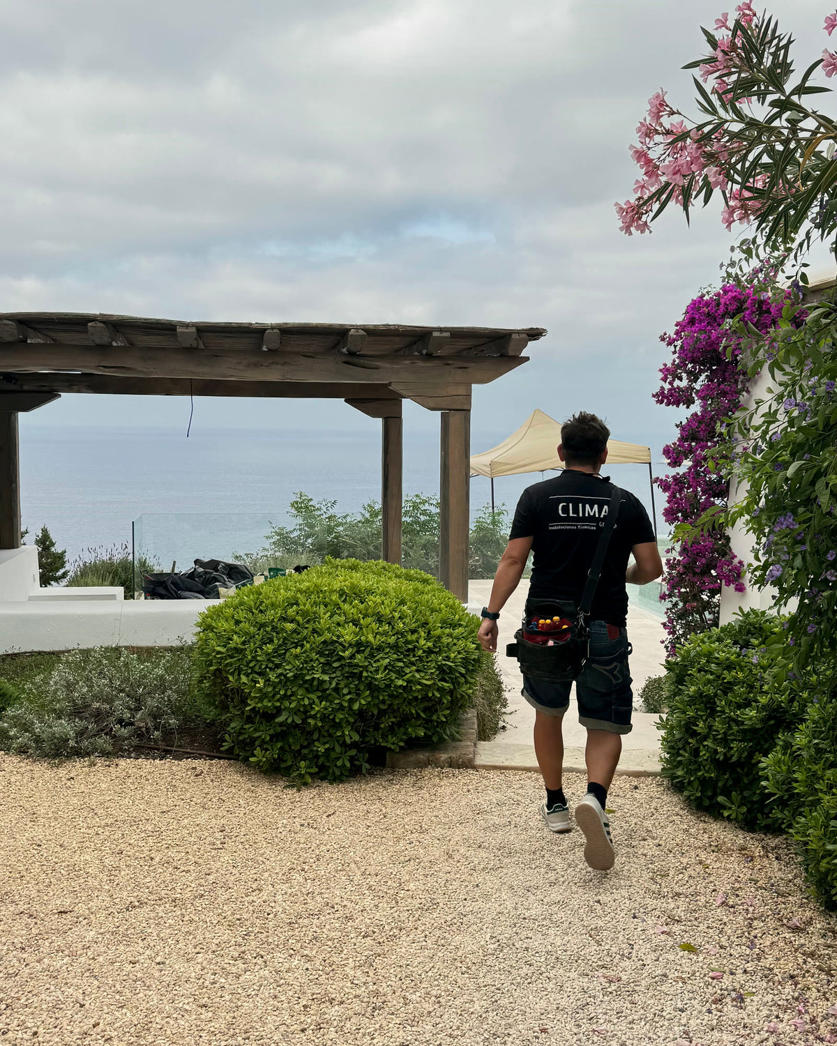 Técnico de CLIMAI accediendo a una villa en Ibiza, con pérgola de sabina y el mar al fondo.